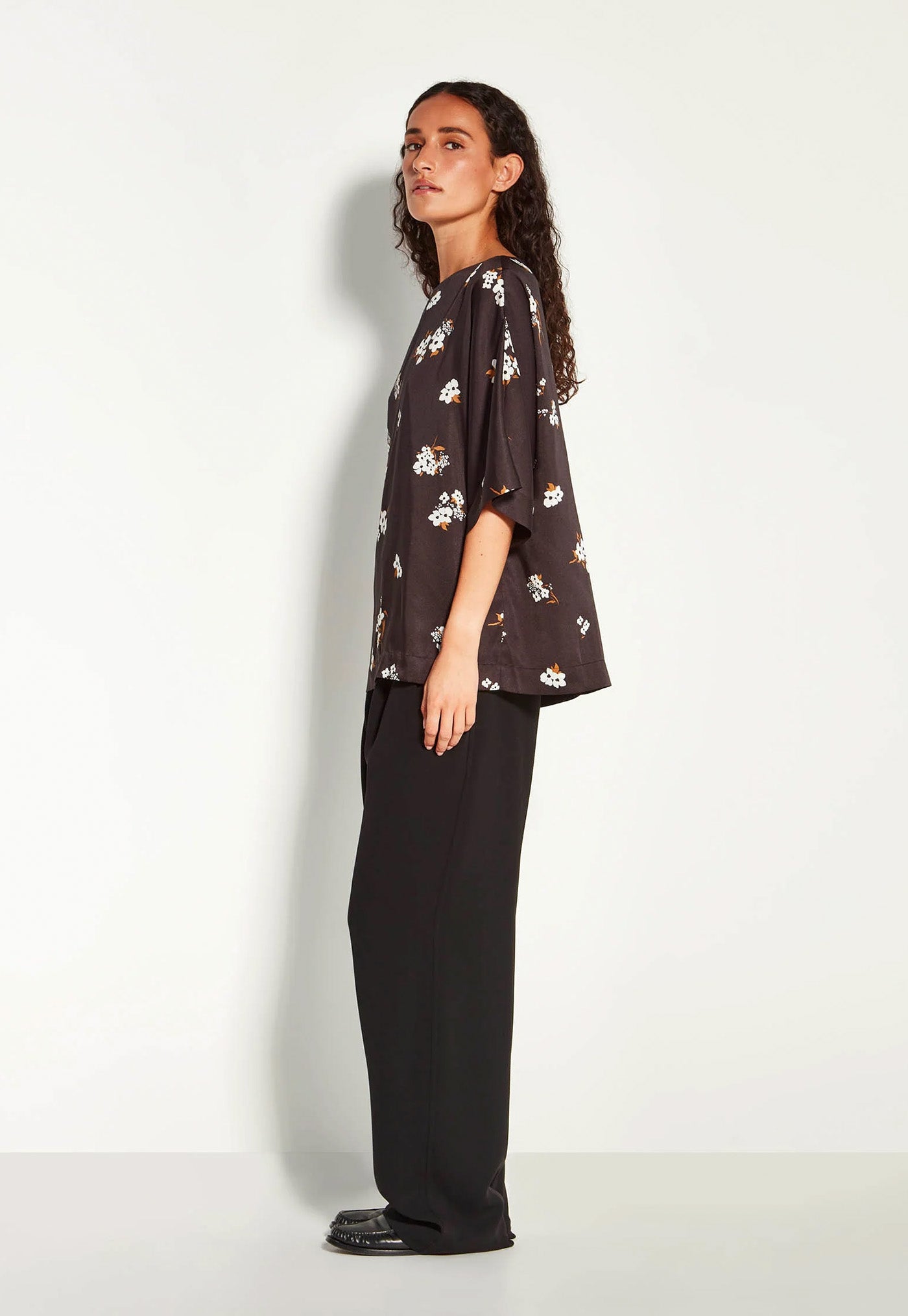 Woman wearing a dark floral blouse and black pants on a white background