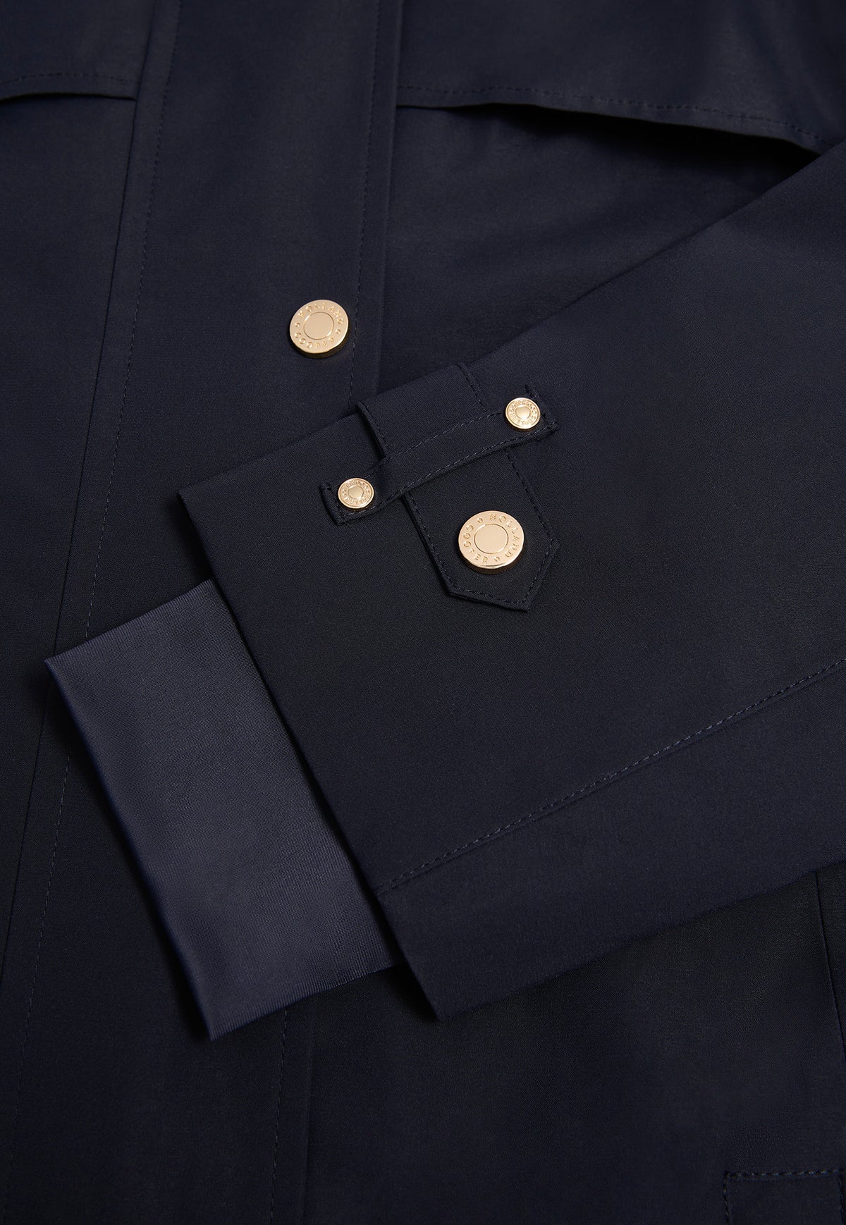 Close-up of a dark navy jacket sleeve with a buttoned cuff and gold-tone snap buttons, set against the dark navy body of the jacket.