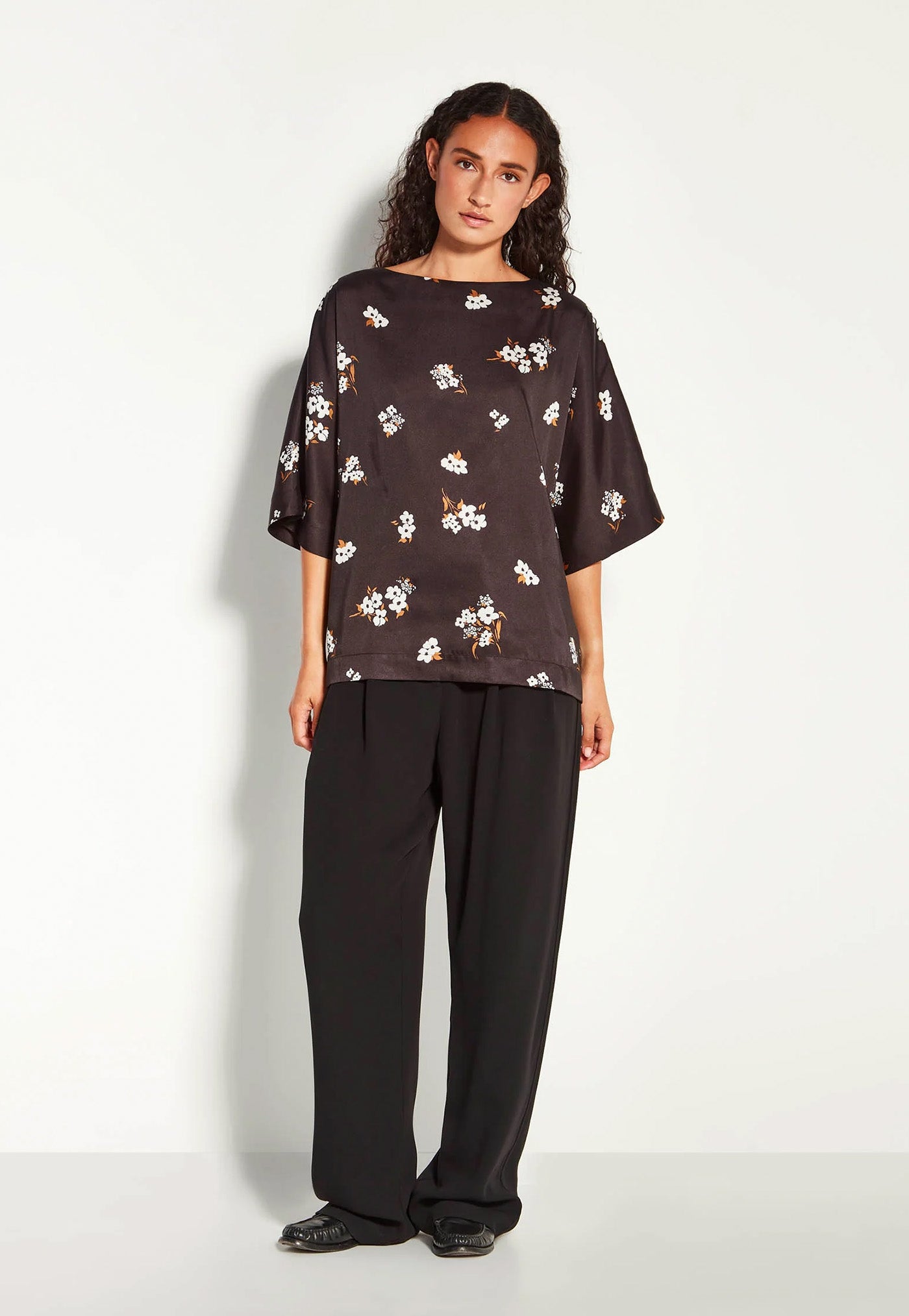 Woman wearing a black floral blouse and black pants on a white background
