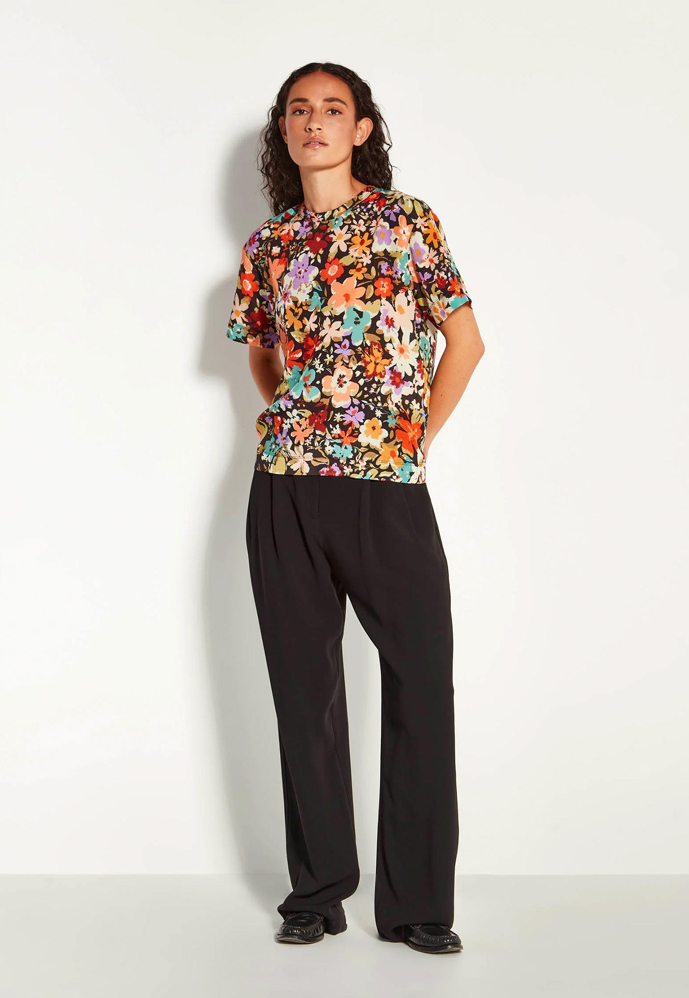 Woman wearing a colorful floral top and black pants on a white background