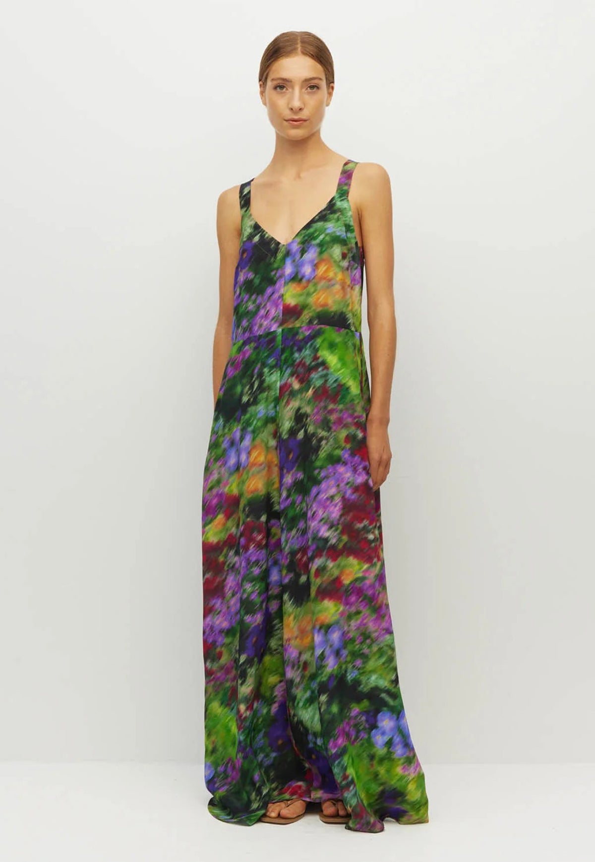 Juliette Hogan sleeveless, floor-length maxi dress with tie waist option and V neck. In a vibrant multicolor abstract floral print in green, purple, orange, and black.