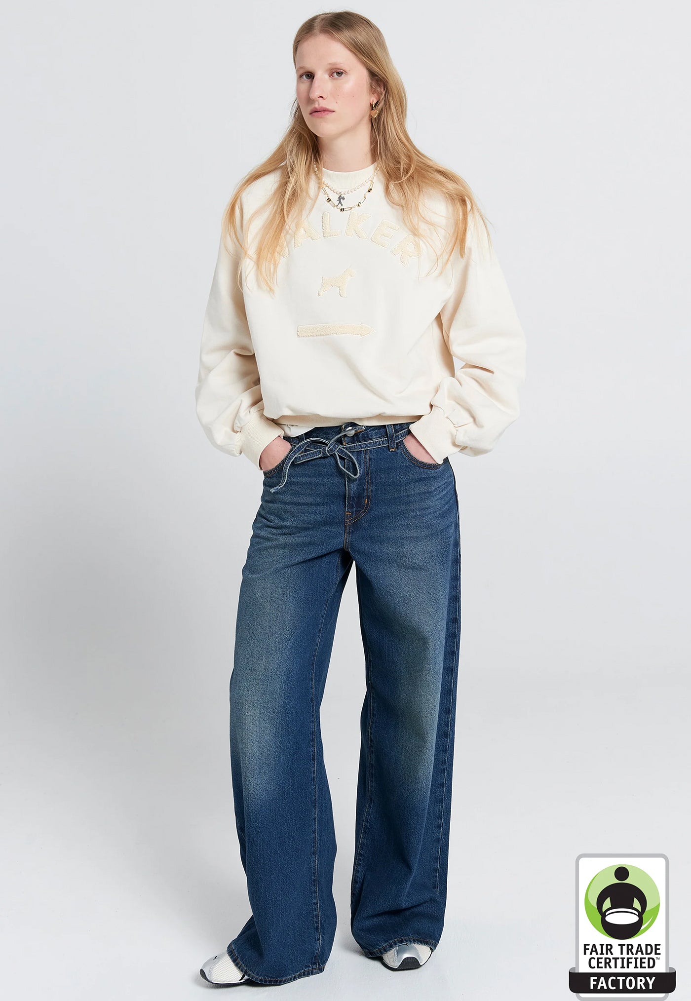 Person wearing a cream sweatshirt and blue jeans on a white background with Fair Trade Factory logo.