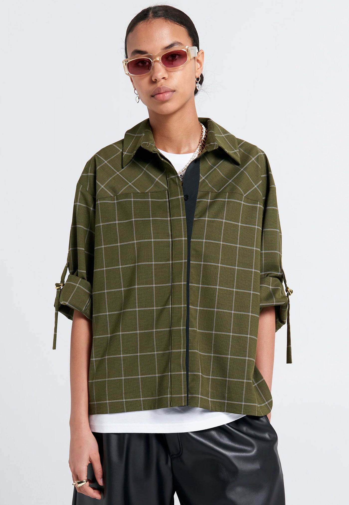 Person wearing a green plaid shirt with rolled-up sleeves on a white background