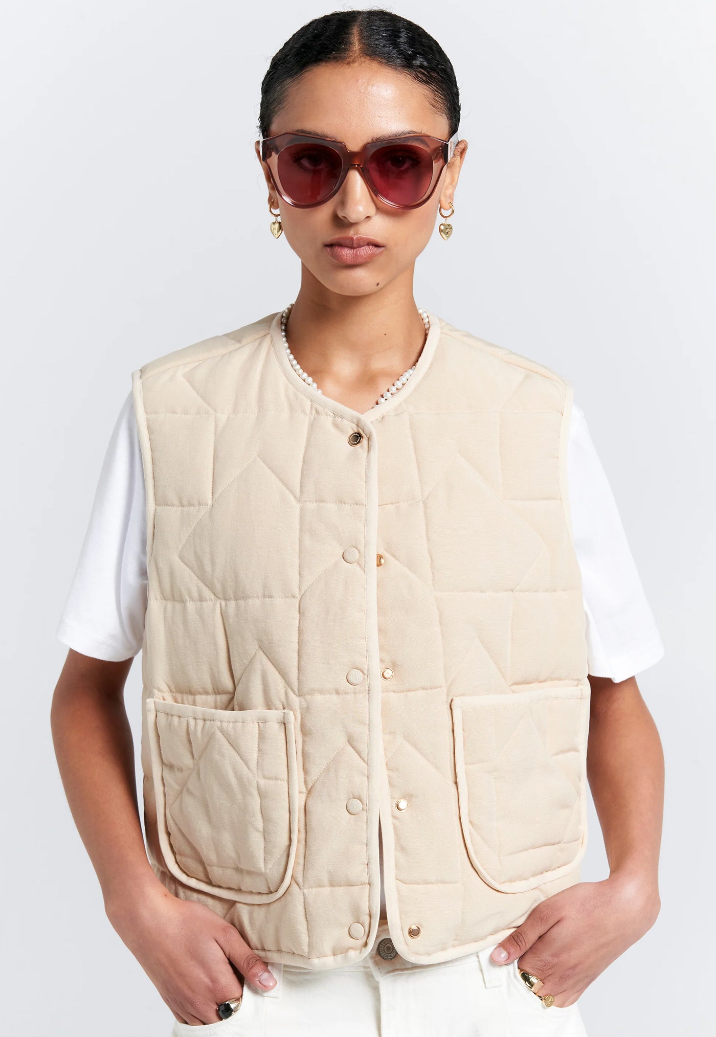Person wearing a beige quilted vest on a white background