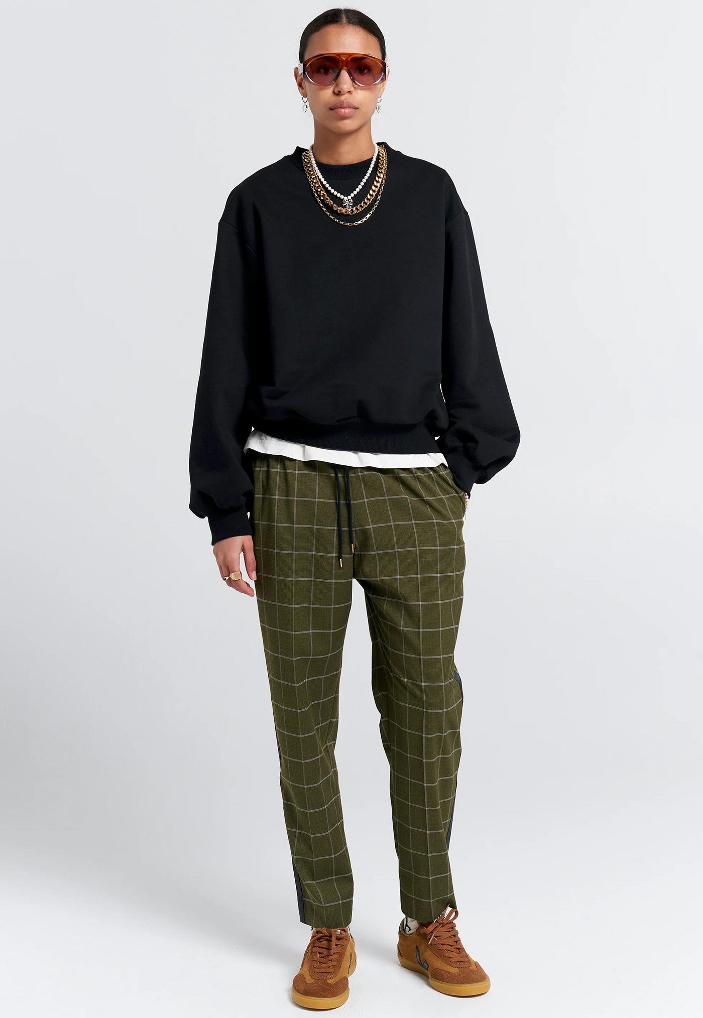 Person wearing a black sweatshirt, green checkered pants, and brown shoes on a white background