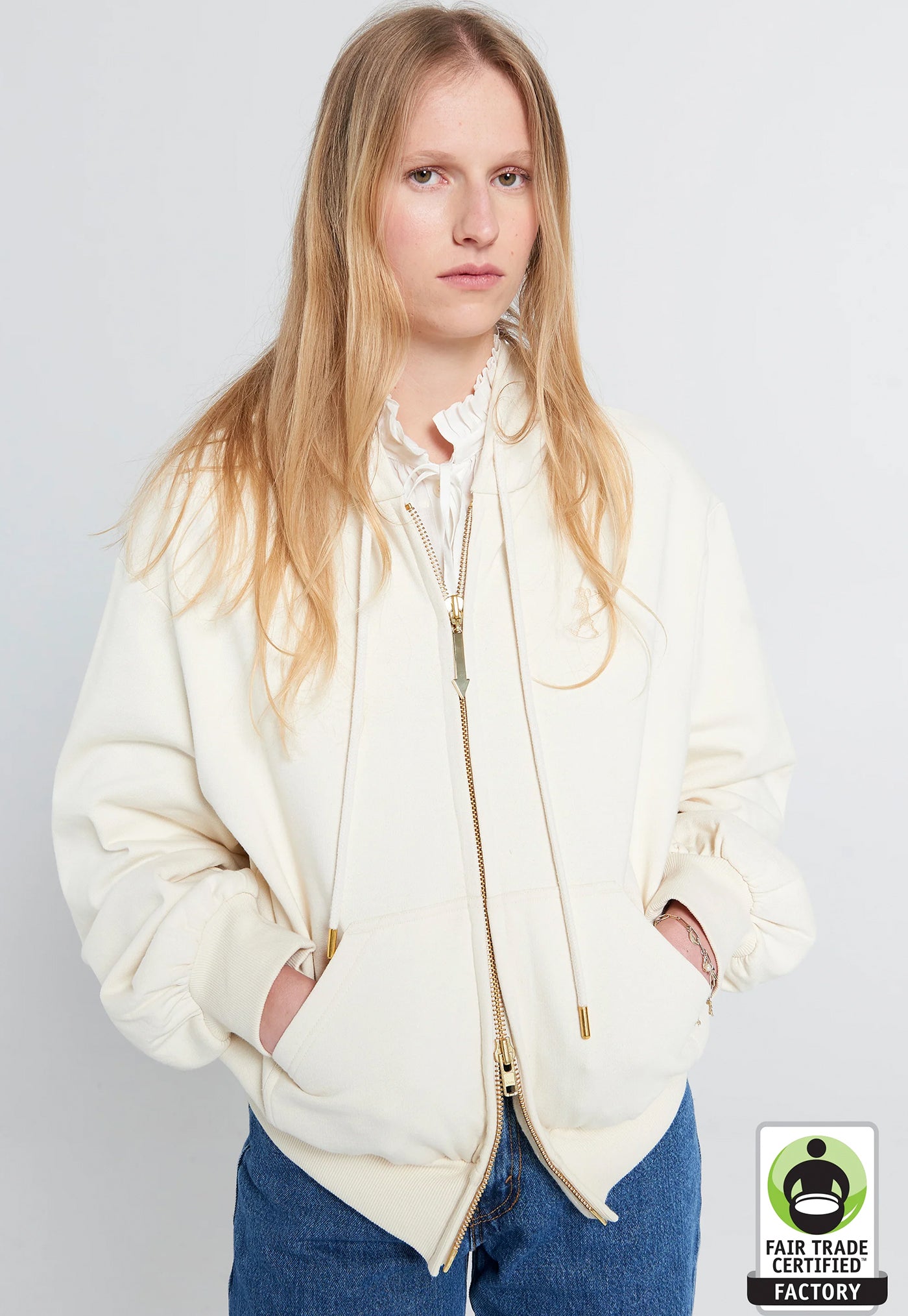 Person wearing a cream-colored hoodie with a visible Fair Trade Certified Factory logo.