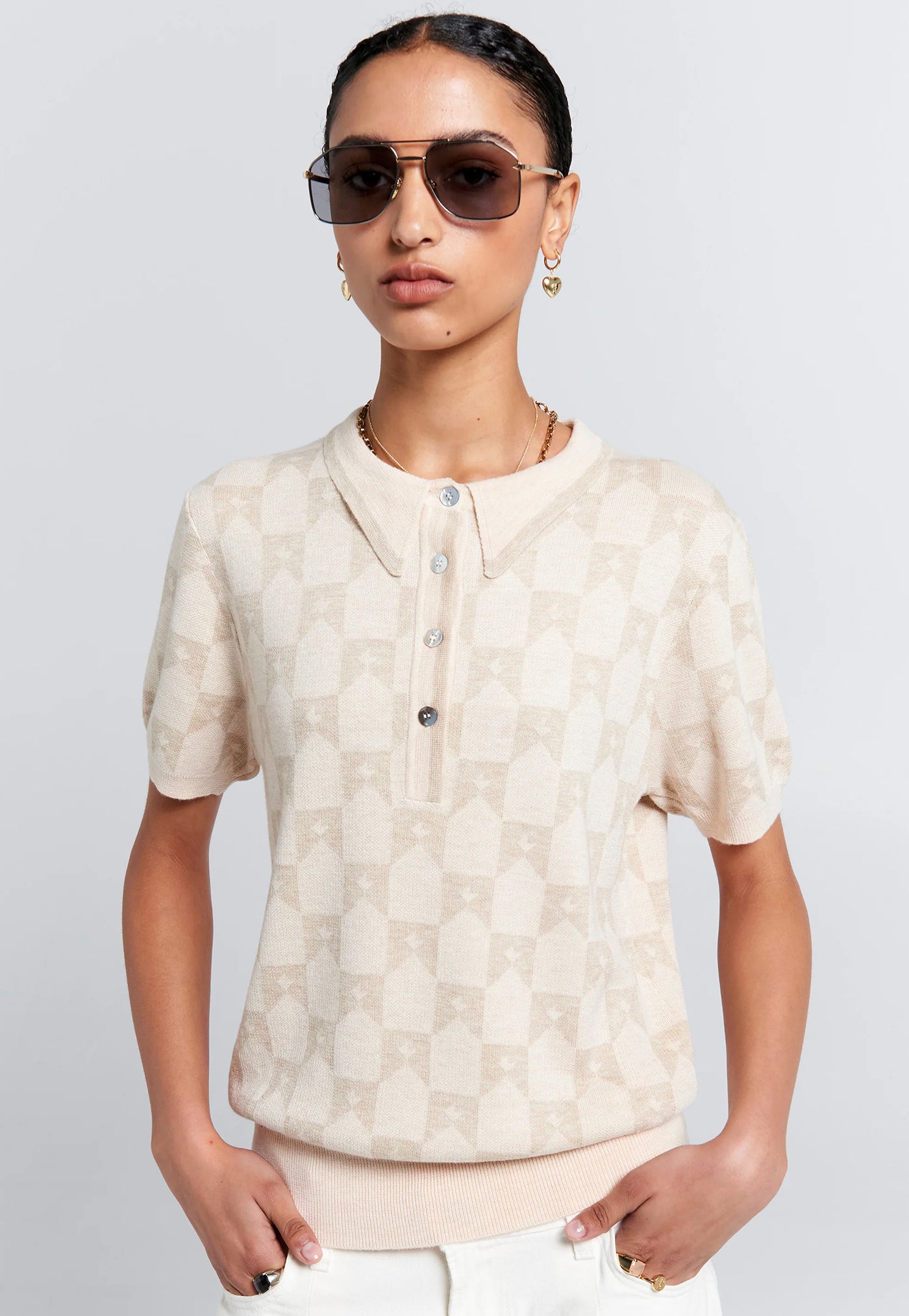 Person wearing a beige patterned shirt and sunglasses on a plain background