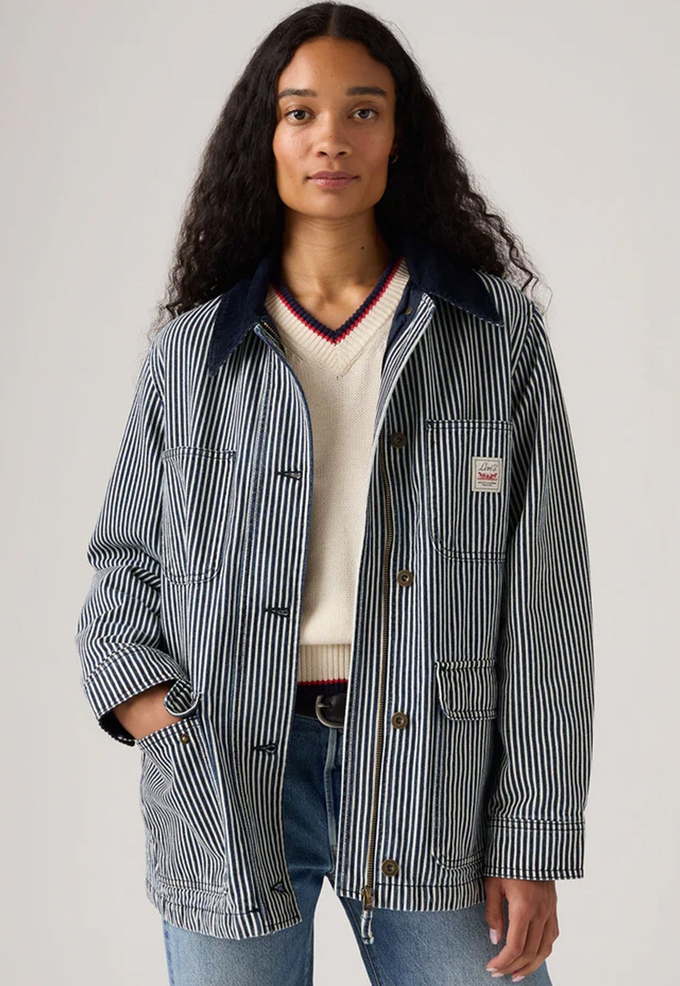 Woman wearing a striped jacket over a sweater and jeans on a plain background