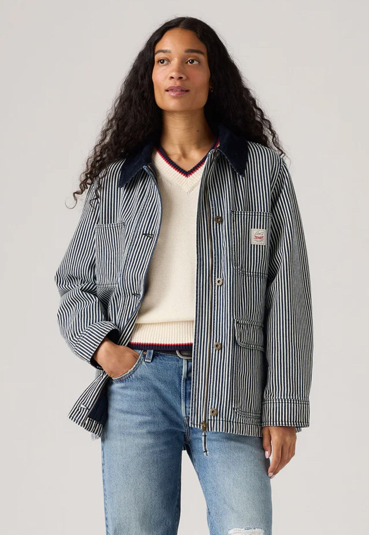 Woman wearing a striped jacket, white shirt, and jeans against a plain background