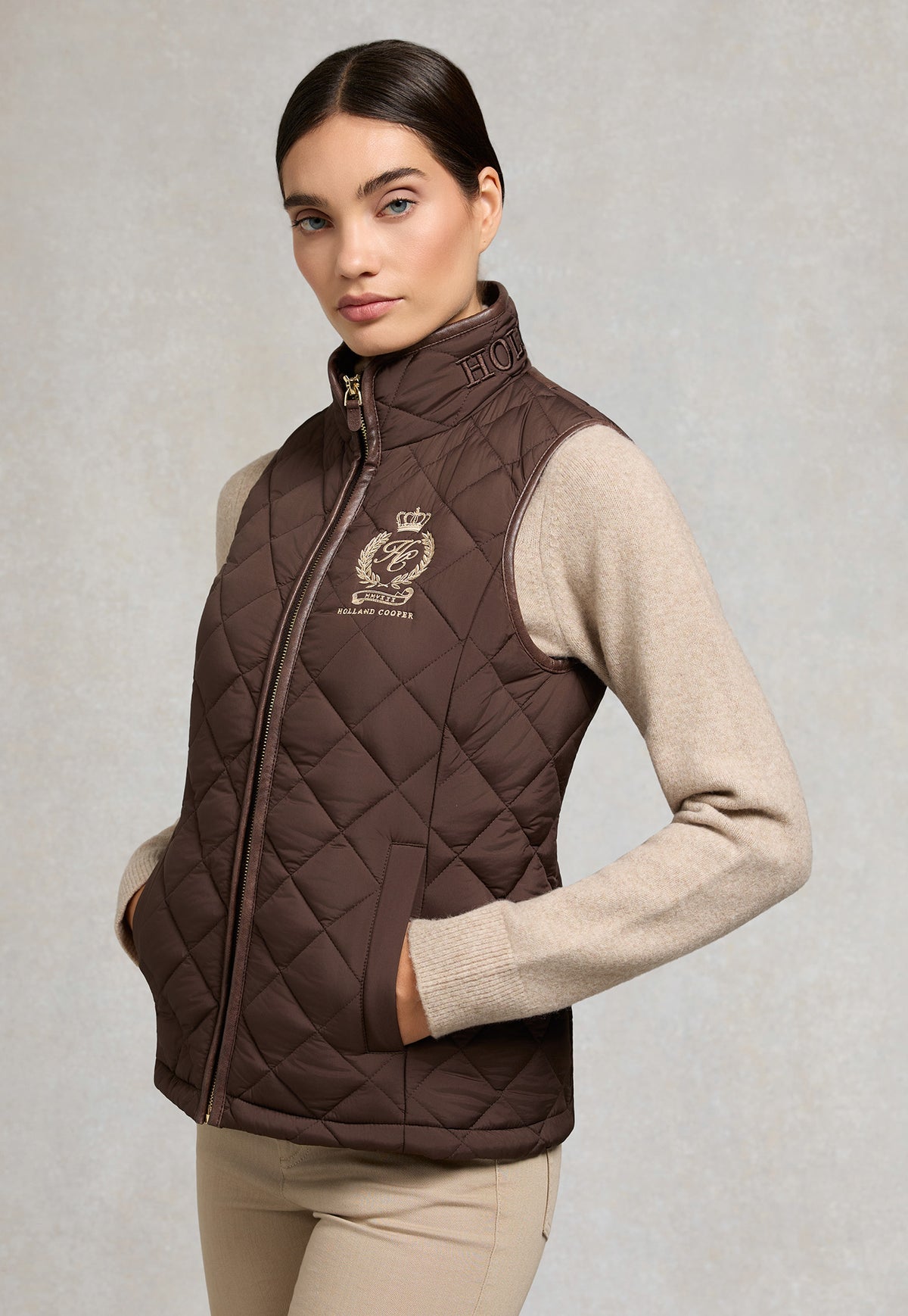 Holland Cooper Lightweight Country Gilet in Chocolate, dark brown diamond quilted gilet with faux leather piping, front zip and crest embroidery.
